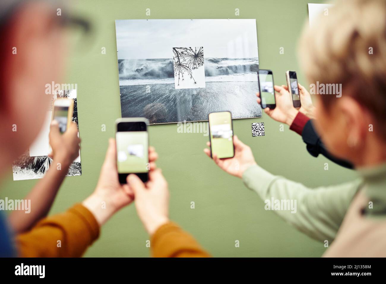 Persone irriconoscibili che eseguono la scansione del codice QR utilizzando gli smartphone per ottenere maggiori informazioni sulla foto sul muro durante la mostra Foto Stock