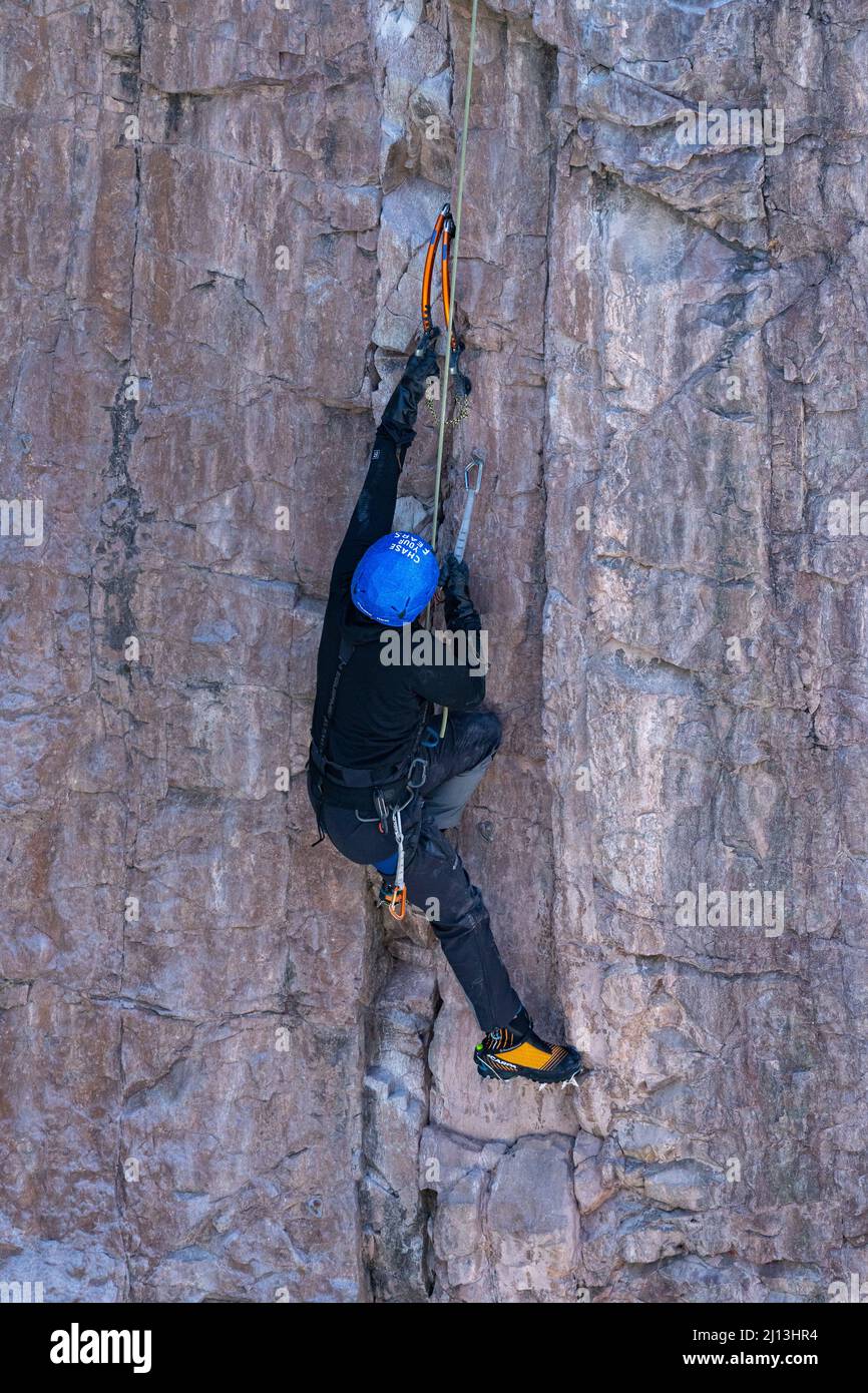 Un arrampicatore sportivo su una scalata mista, utilizzando assi di ghiaccio e ramponi per scalare una parete di roccia nel Parco di ghiaccio di Ouray in Colorado. La sezione di roccia è circondata Foto Stock