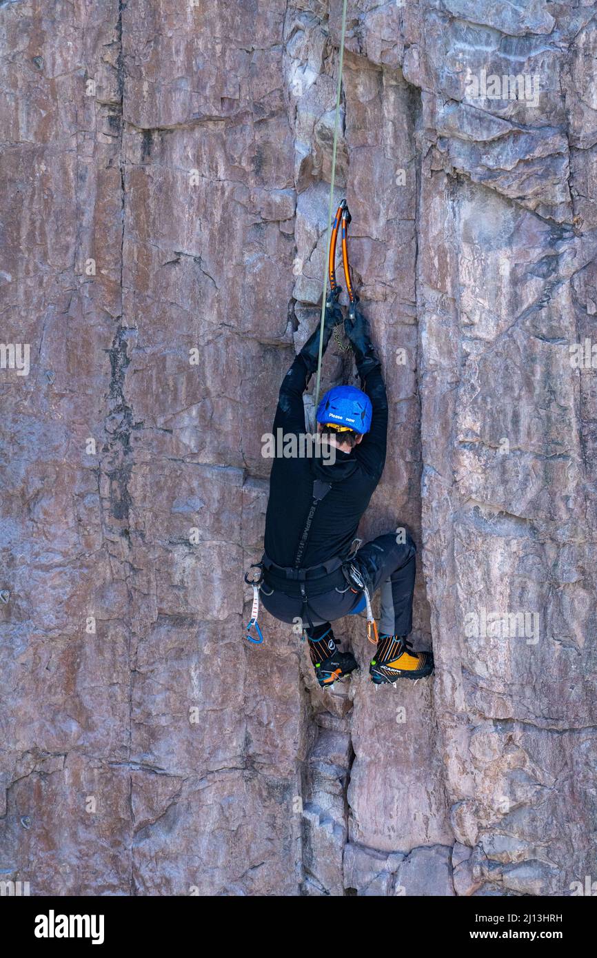 Un arrampicatore sportivo su una scalata mista, utilizzando assi di ghiaccio e ramponi per scalare una parete di roccia nel Parco di ghiaccio di Ouray in Colorado. La sezione di roccia è circondata Foto Stock