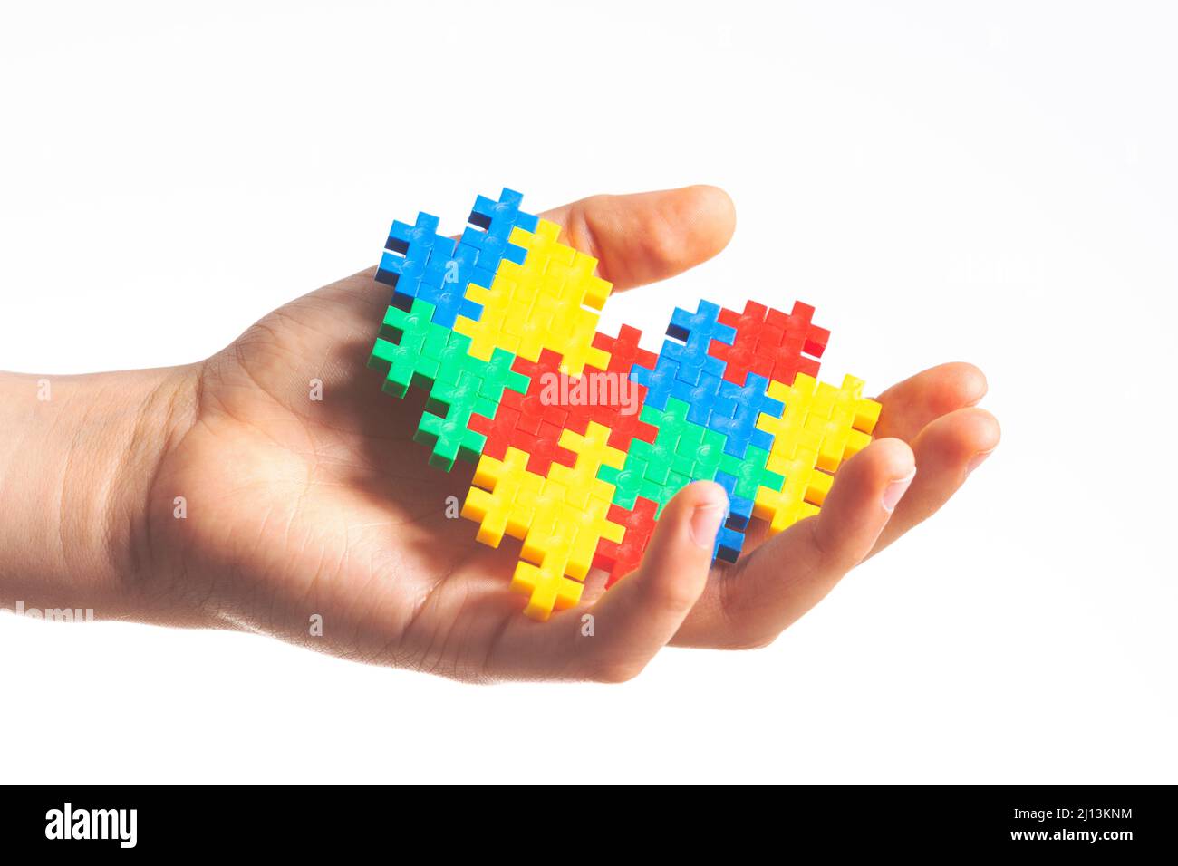 Le mani del bambino che tengono il cuore colorato del puzzle su sfondo bianco. Concetto di giornata di consapevolezza autismo mondiale Foto Stock