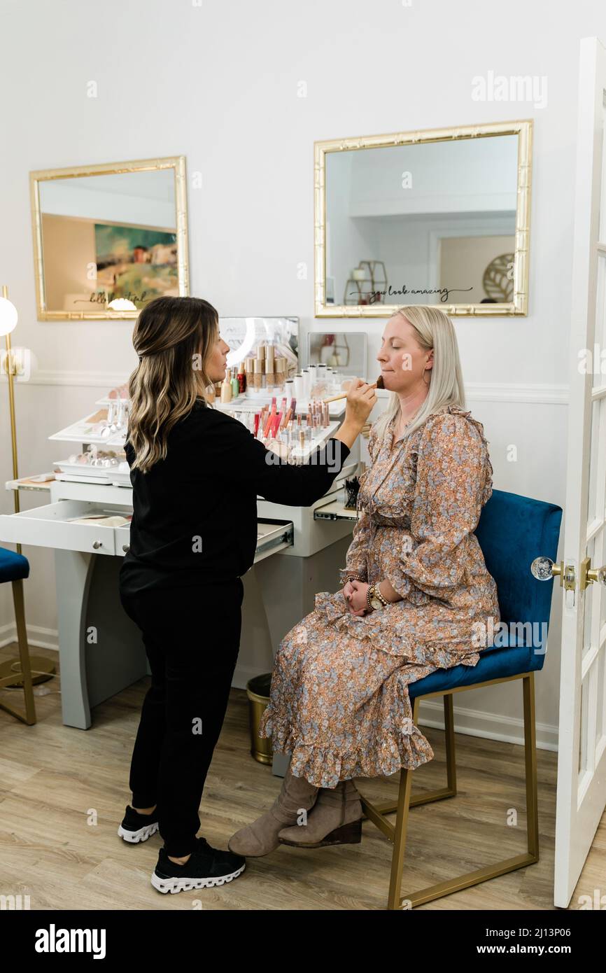 Cosmetologist che applica il trucco di fondazione ad una donna bionda in una sedia di trucco Foto Stock