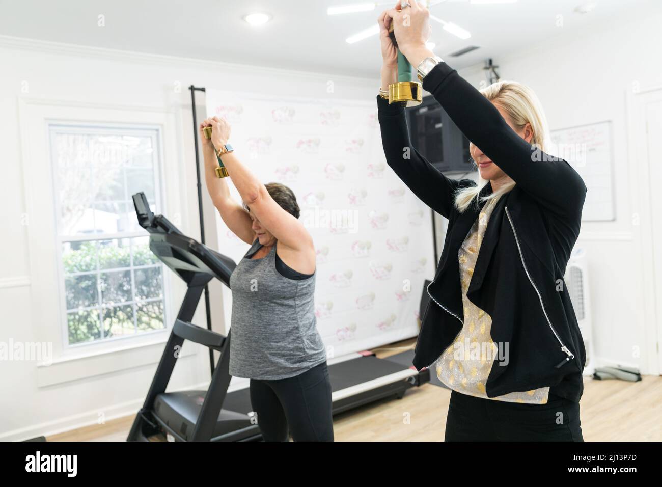 Un personal trainer femminile che aiuta un cliente esercizio fisico, addestrare, e costruire il muscolo utilizzando piccoli pesi a mano in una palestra Foto Stock