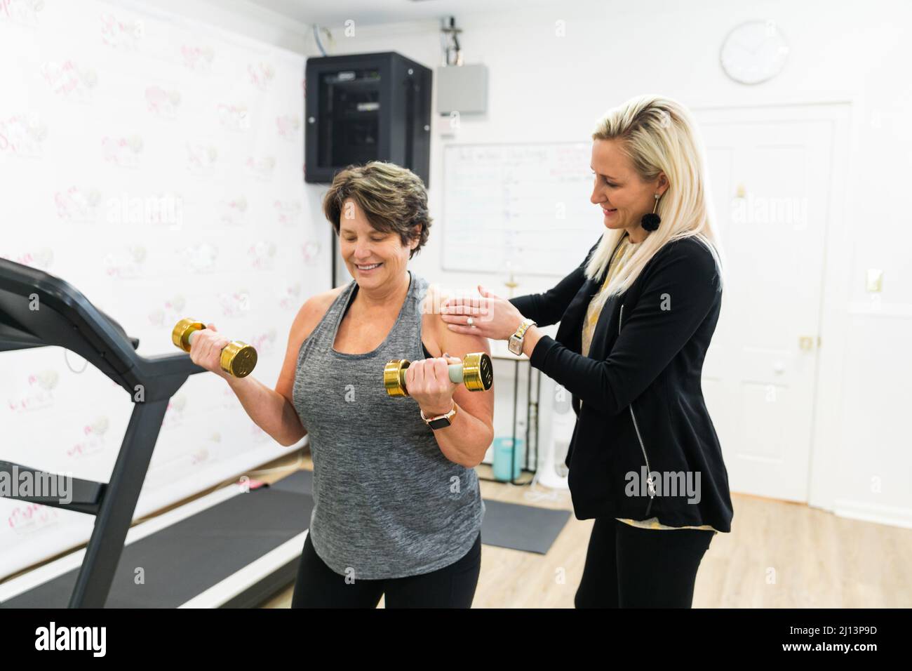 Un personal trainer femminile che aiuta un cliente esercizio fisico, addestrare, e costruire il muscolo utilizzando piccoli pesi a mano in una palestra Foto Stock