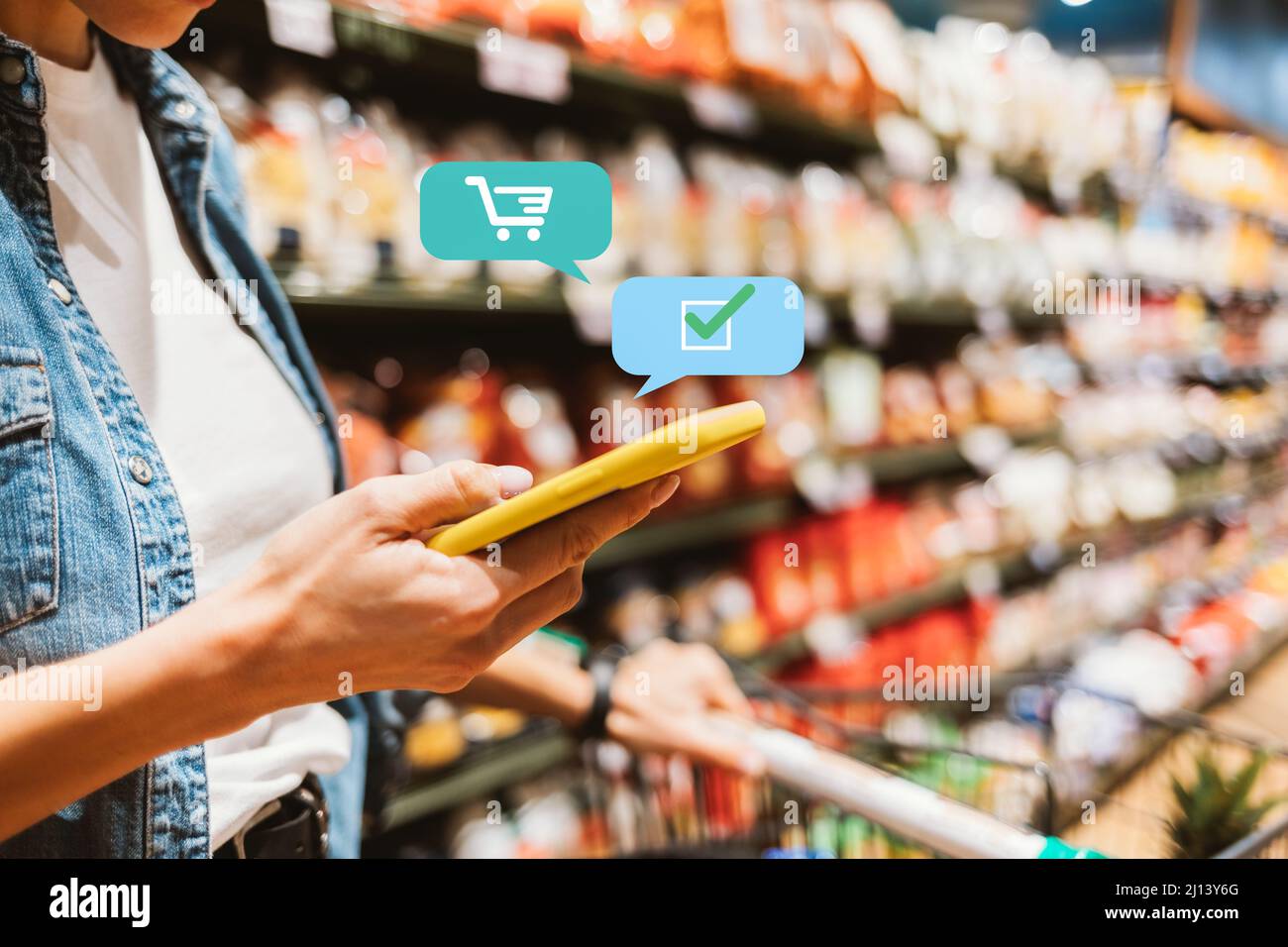 Shopping list app concept, primo piano giovane donna in supermercato con il suo smartphone per marcare i prodotti di cui ha bisogno Foto Stock