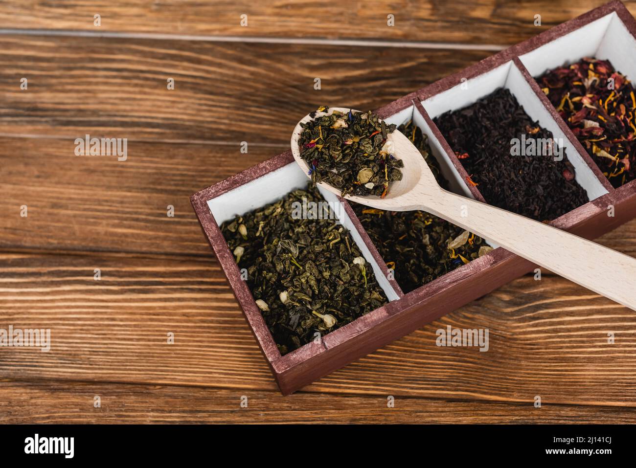 Vista dall'alto del tè secco su cucchiaio e scatola su superficie di legno Foto Stock