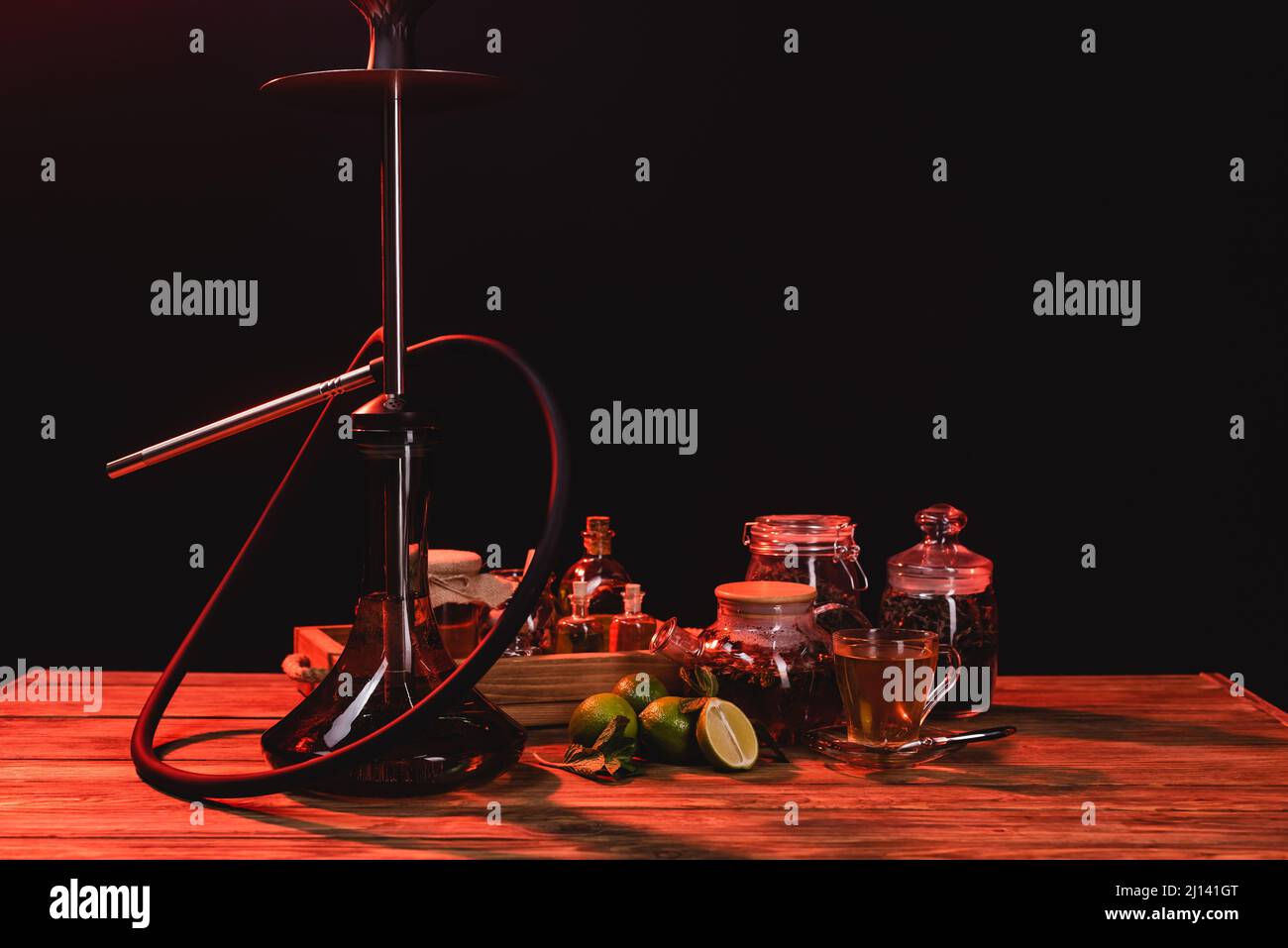 Tè, lime fresche e hookah su tavola di legno isolato su nero con luce rossa Foto Stock