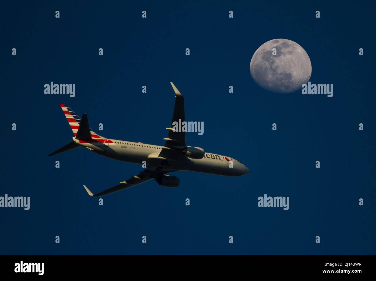 Un jet commerciale American Airlines passa sotto una luna piena al tramonto. Foto Stock