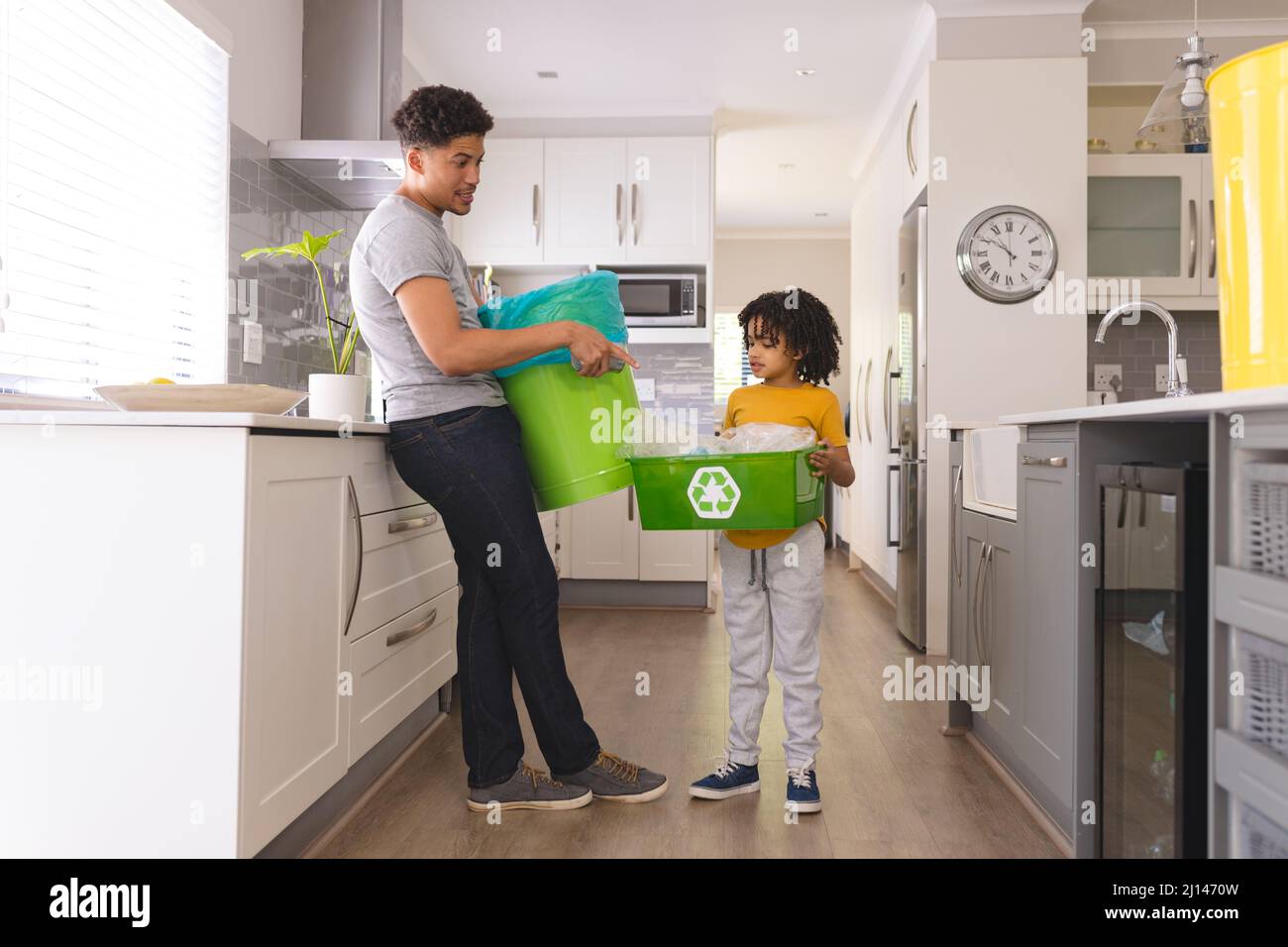 Un uomo ispanico che insegna a figlio sulla gestione dei rifiuti mentre si trova in cucina a casa Foto Stock