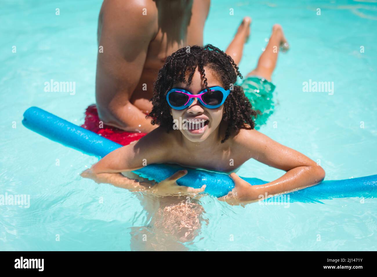 Uomo ispanico aiutare il figlio a nuotare con galleggiante in piscina in giorno di sole Foto Stock