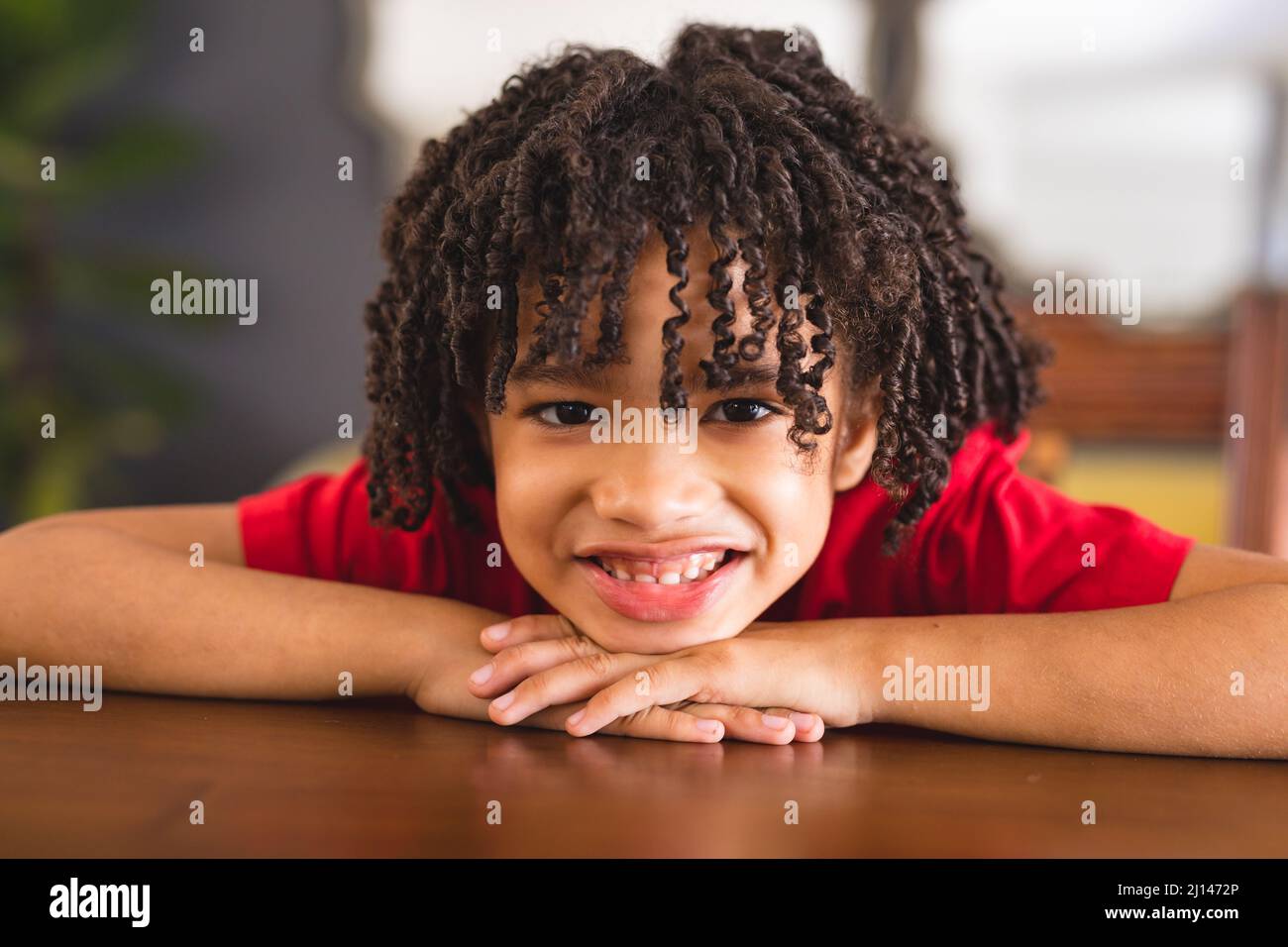 Ritratto di felice ragazzo ispanico con capelli ricci neri appoggiati sul tavolo a casa Foto Stock