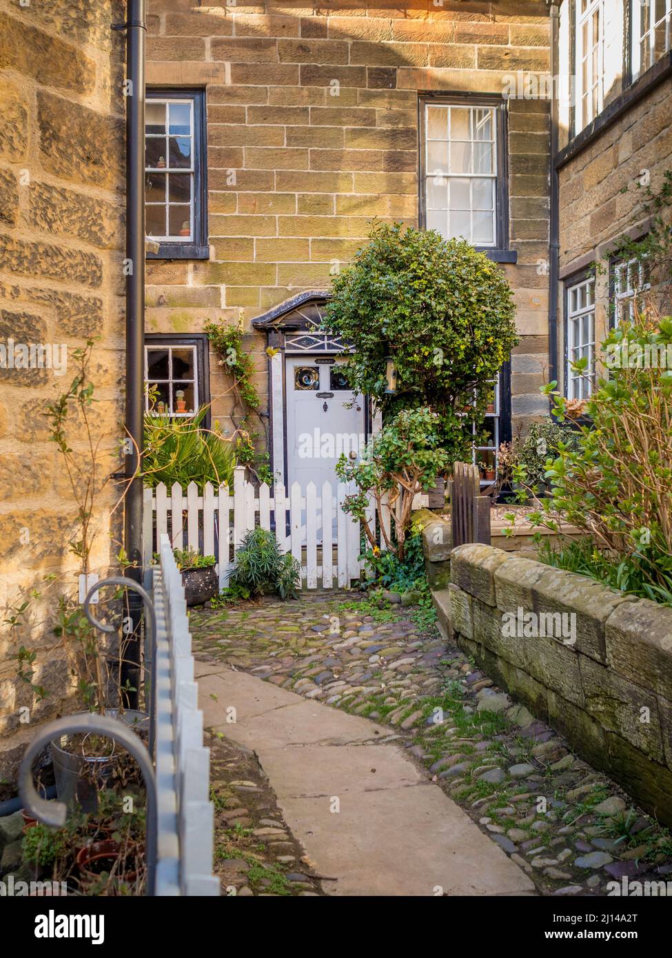 Tradizionale cottage costruito in pietra con recinto bianco picket, situato in uno stretto vicolo posteriore nella città vecchia di Robin Hoods Bay, North Yorkshire. Foto Stock