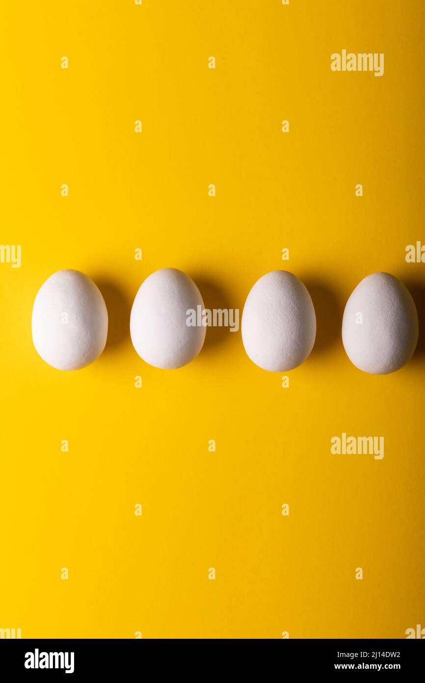 Direttamente sopra la vista delle uova bianche fresche disposte fianco a fianco su sfondo giallo Foto Stock