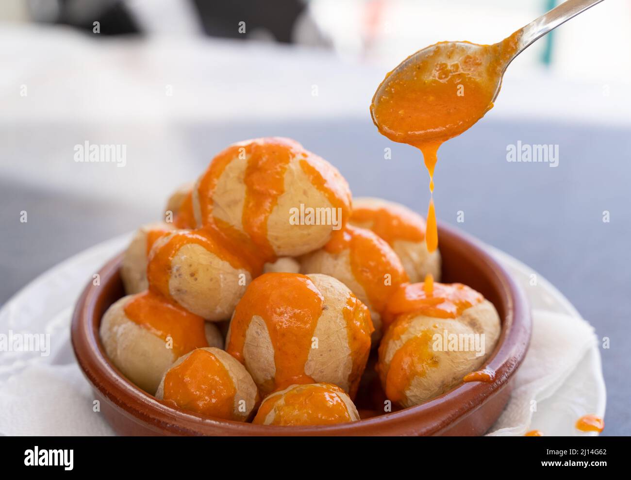 Versare la salsa mojo piccante su papas arrugadas in un piatto di argilla. Tradizionale rughe patate snack cibo da Gran Canaria isola, Spagna Foto Stock