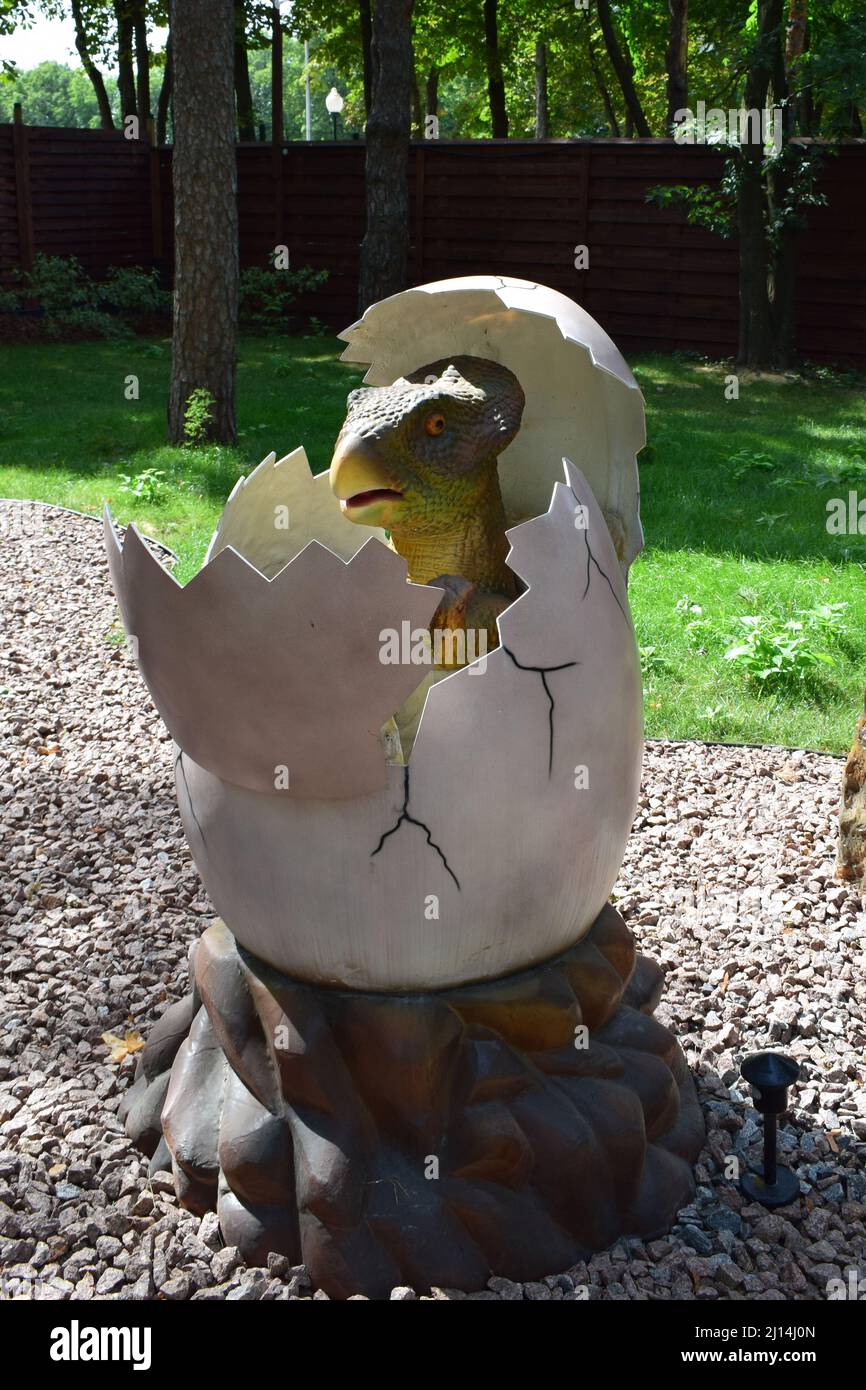 DINO PARK, KHARKOV - 8 AGOSTO 2021: Statua del dinosauro nel parco forestale in natura per sfondo. Un piccolo dinosauro si schiusa da un uovo. La preistoria Foto Stock