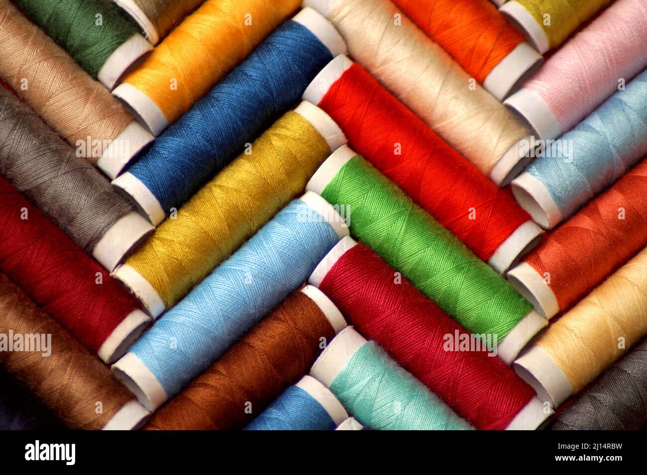 le bobine di filo da cucito multicolore giacciono in un modello a spina di pesce Foto Stock