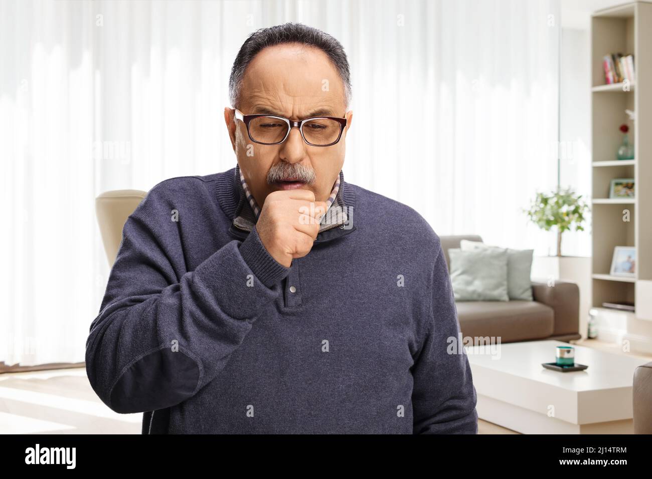 Uomo maturo che tosse a casa in un soggiorno Foto Stock