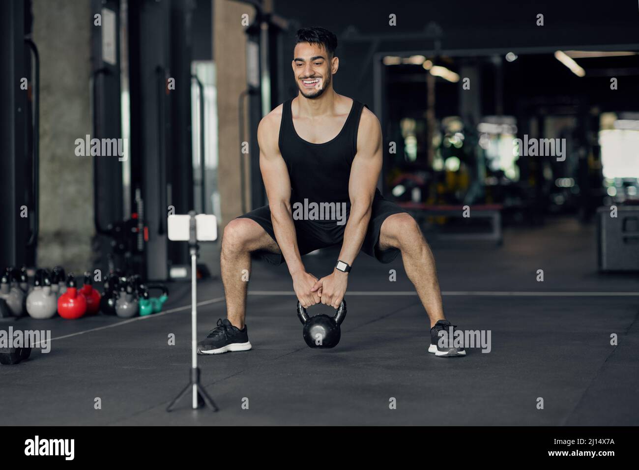 Atleta maschile mediorientale che cattura gli allenamenti online in palestra per il blog di fitness Foto Stock