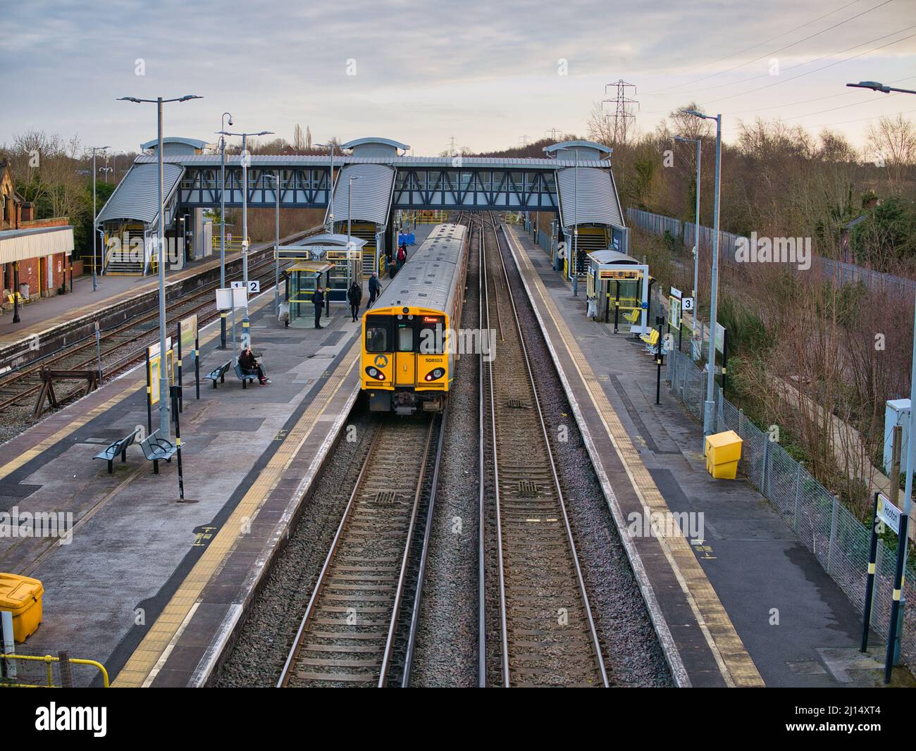 Binari e piattaforme ferroviarie presso la stazione di Hooton a Wirral, Inghilterra nord-occidentale, Regno Unito. Un singolo treno pendolari attende alla piattaforma per i pendolari ad ali Foto Stock