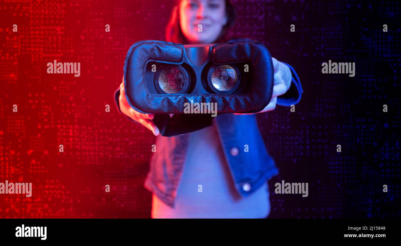 Donna ispanica che mostra i suoi occhiali per realtà virtuale con tecnologia digitale in primo piano con sfondo digitale con luce blu e rossa Foto Stock