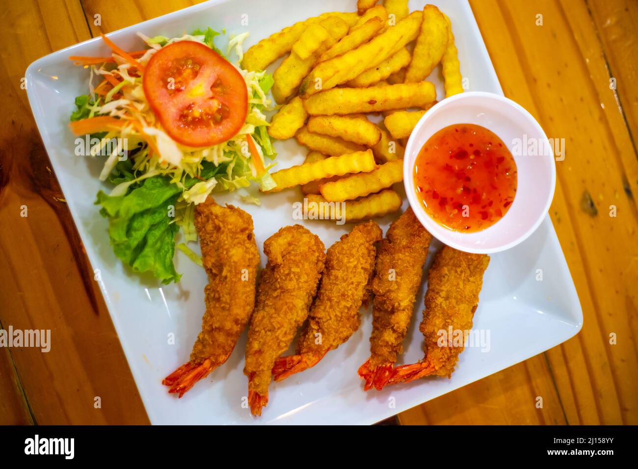 Sul tavolo c'è un piatto di gamberi in pastella, patatine fritte e un'insalata di verdure. Piatti a base di pesce. Foto Stock