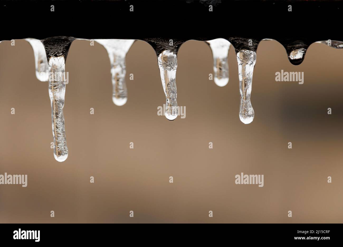 goccioline d'acqua congelate appese sotto una guida metallica grintosa con crepe e inclusioni visibili, su sfondo beige morbido con spazio di copia Foto Stock