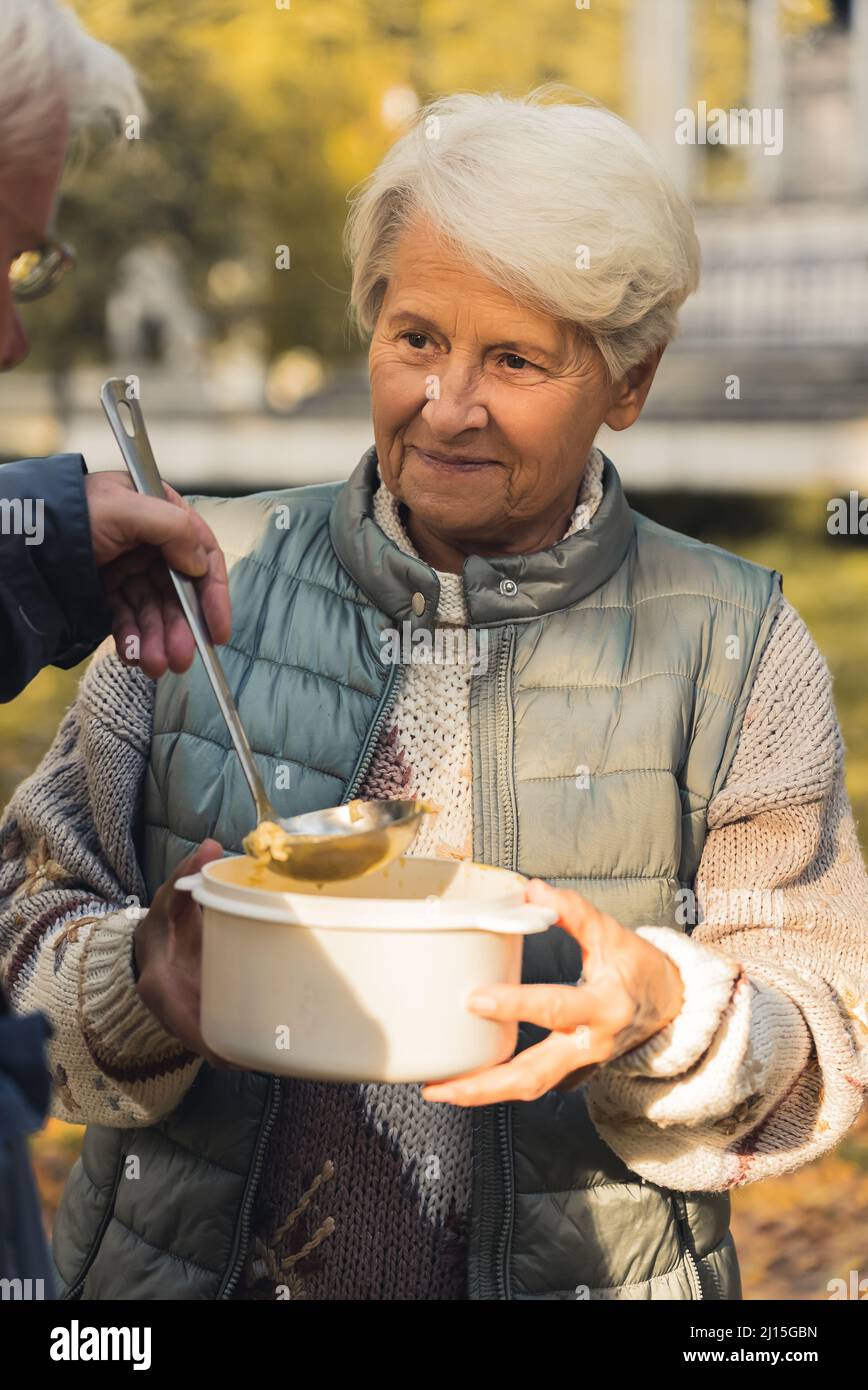 Donna caucasica anziana in abbigliamento casual riceve cibo da un uomo, guarda l'uomo sfondo parco persone anziane benessere sostegno concetto medio shot fuoco selettivo . Foto di alta qualità Foto Stock