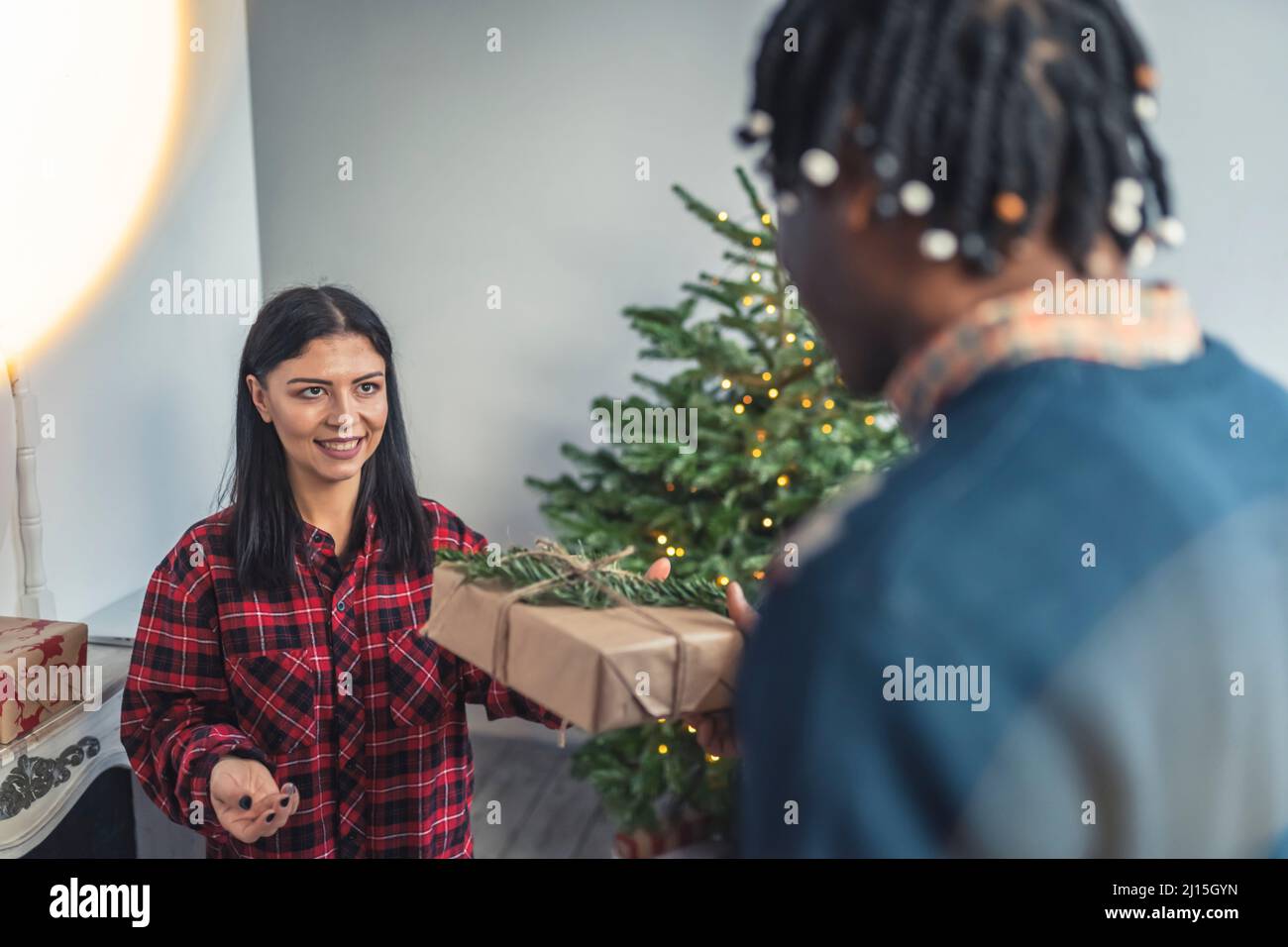 L'uomo afroamericano sorprende la moglie caucasica con un regalo di Natale. Concetto di coppia interrazziale. Foto di alta qualità Foto Stock