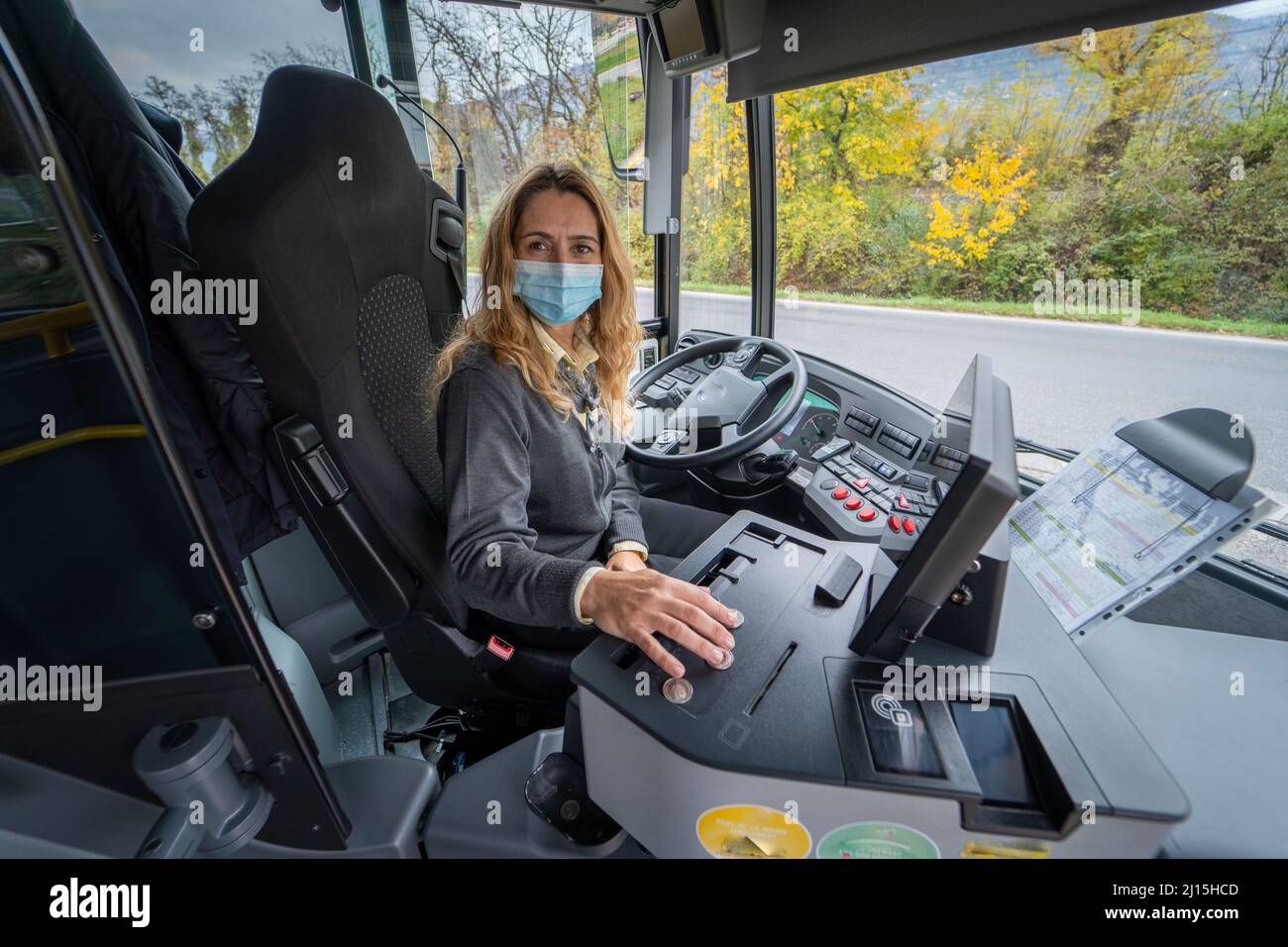 Sorridente conducente di autobus con una maschera che stampa un biglietto Foto Stock