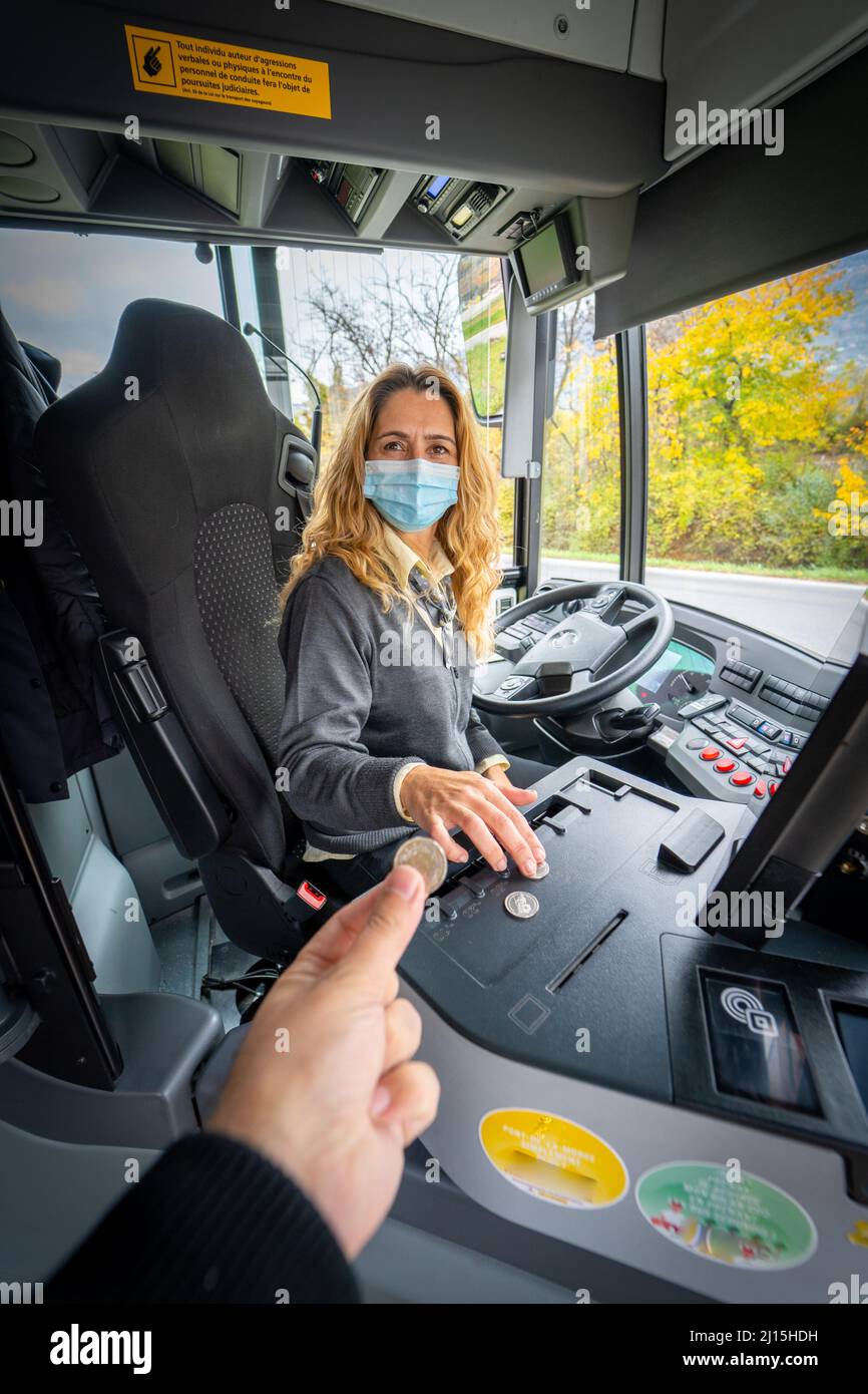 Colpo verticale di una mano che paga una moneta ad un driver del bus femminile in una maschera Foto Stock