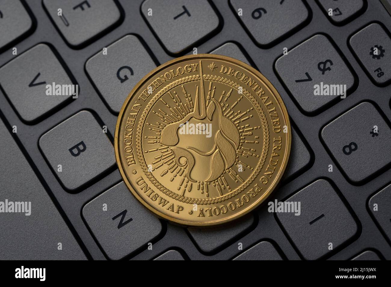 Uniswap UNI Cryptocurrency Physical Coin posizionato sulla tastiera del computer e illuminato con luce soffusa. Foto Stock