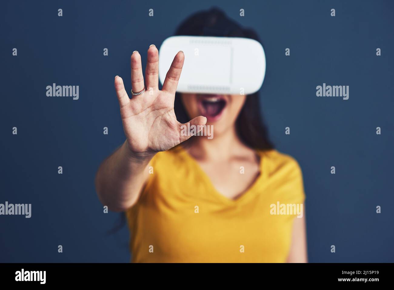 Cambiare il volto della realtà. Ritratto da studio di una giovane donna che indossa un visore VR su sfondo blu. Foto Stock