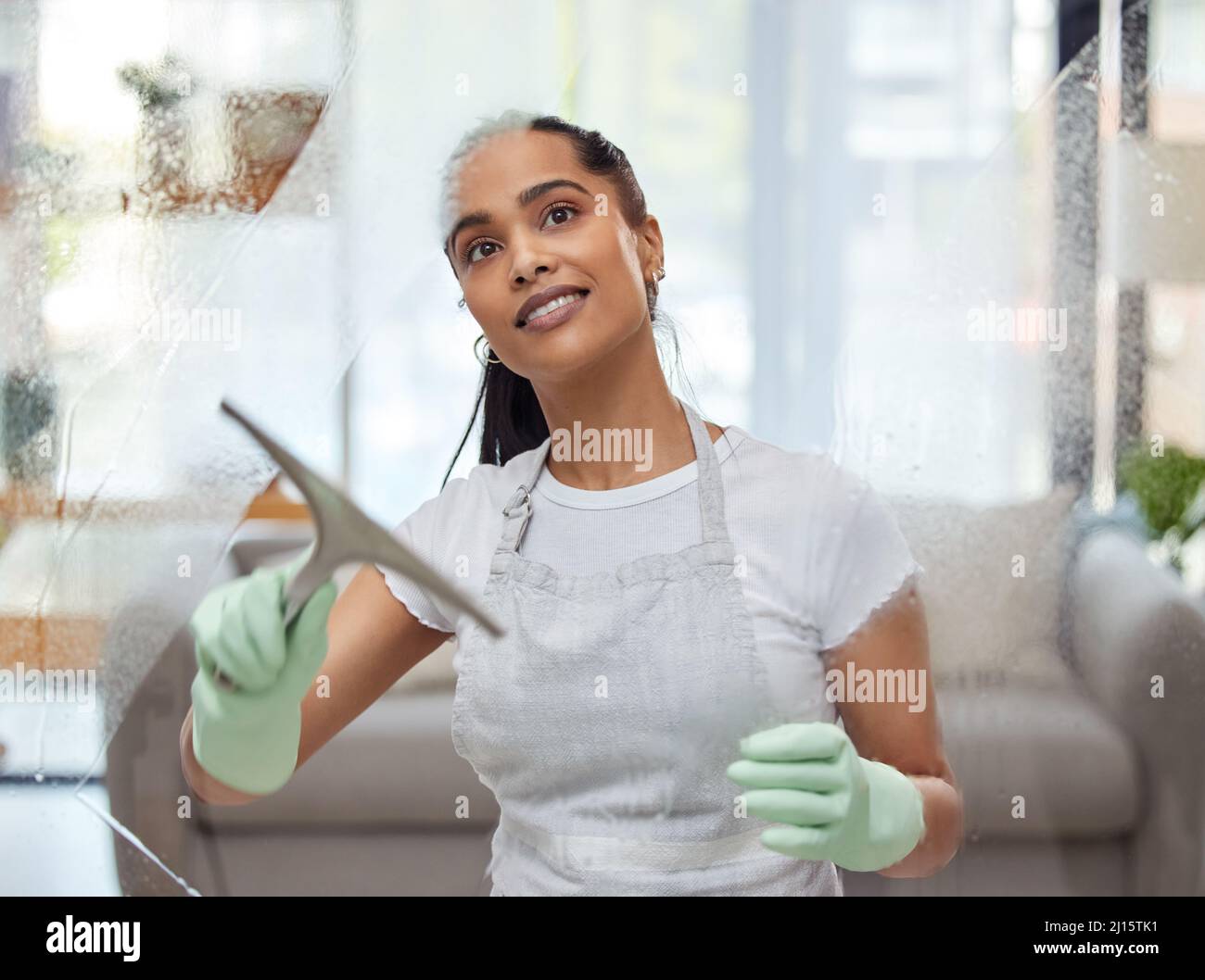 Mi piace le mie finestre chiaro come cristallo. Scatto di una giovane donna attraente in piedi da sola a casa e la pulizia delle sue finestre. Foto Stock