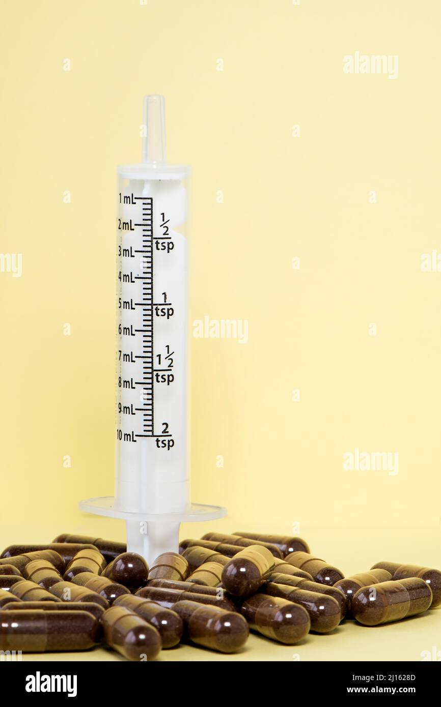 Siringa senza ago e pillole marroni su sfondo giallo. Concetto medico. Foto Stock