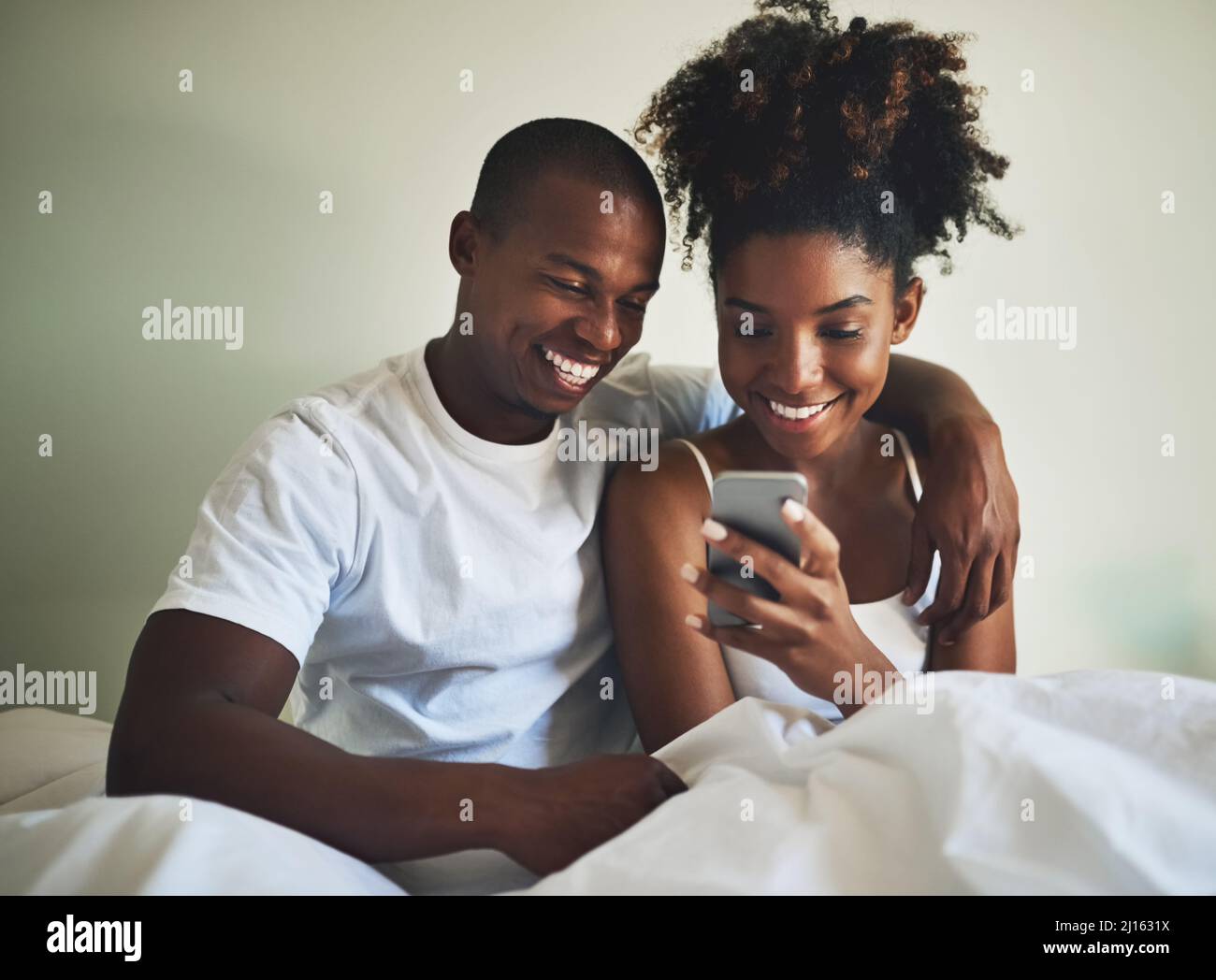 Niente dice amore come un account di social media congiunto. Scatto di una giovane coppia felice usando un telefono cellulare insieme a letto a casa. Foto Stock