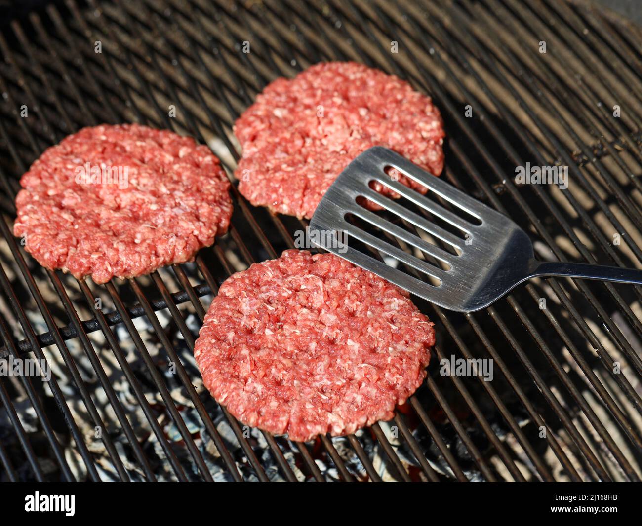 vista dall'alto delle polpette di hamburger di manzo crudo sulla griglia grigliata con spatola Foto Stock