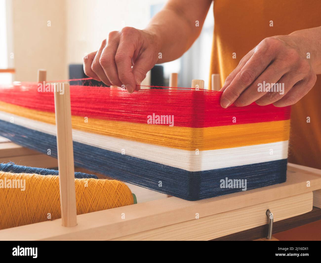 Weaver sta avvolgendo un ordito per tessitura usando il telaio di orditura, fuoco selettivo Foto Stock
