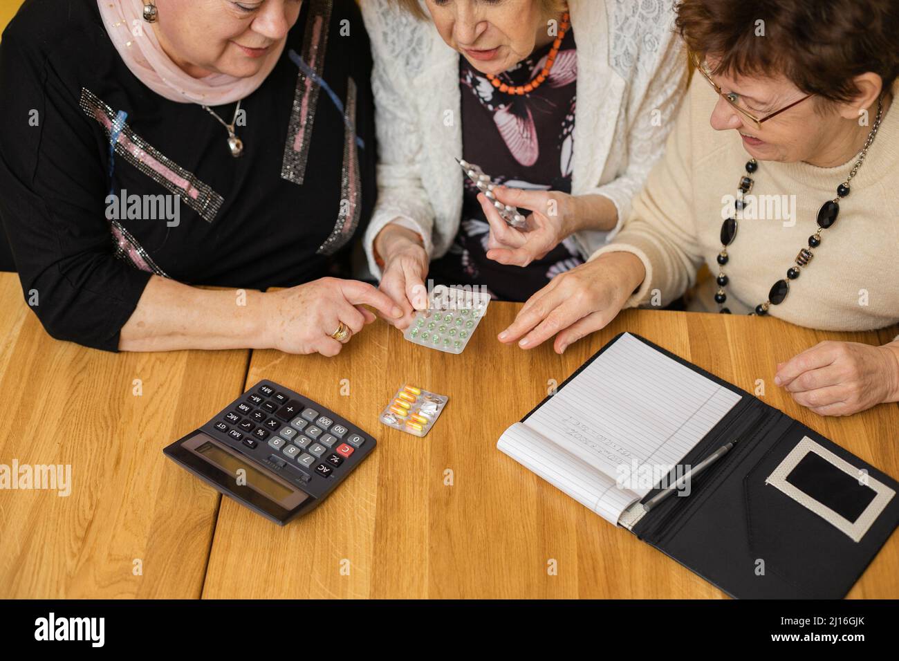 Vista dall'alto di tre donne anziane assorbite che guardano i tablet, seduti a un tavolo di legno con notebook con penna, calcolatrice. Foto Stock