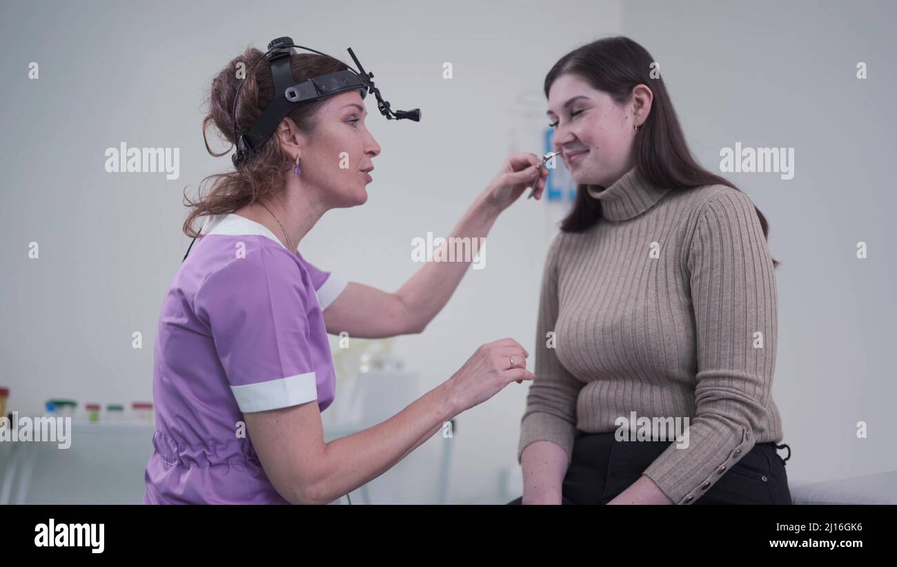 Concetto di otolaringologia. Otorhinolaringologist donna positiva che controlla il naso con otoscopio del suo paziente in ospedale. Congestione nasale, sinusite Foto Stock