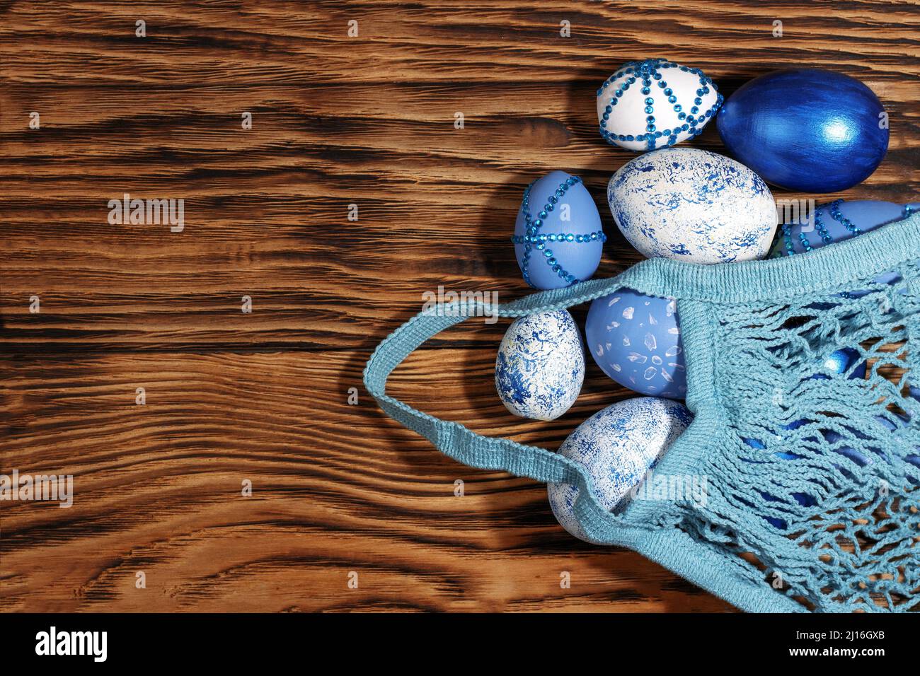 Blu, bianco, con rhinestones uova di Pasqua in un sacchetto di stringa su un fondo di legno giallo trendy. Il concetto minimo di Pasqua. Vista dall'alto. Carta di Pasqua w Foto Stock