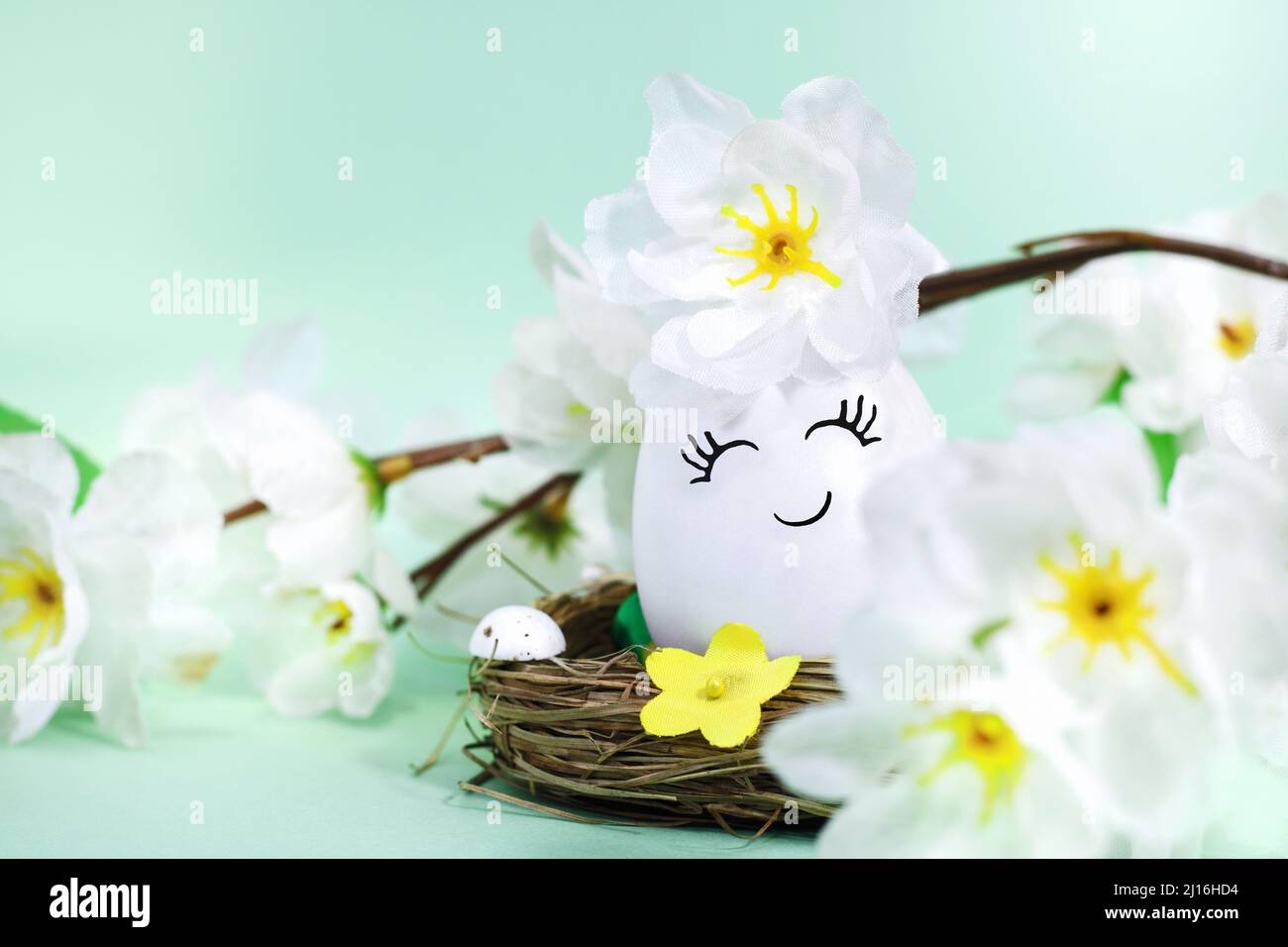 Un uovo di Pasqua decorato felice o carino in un cestino, con fiori su sfondo verde. Cartolina di Pasqua. Foto Stock