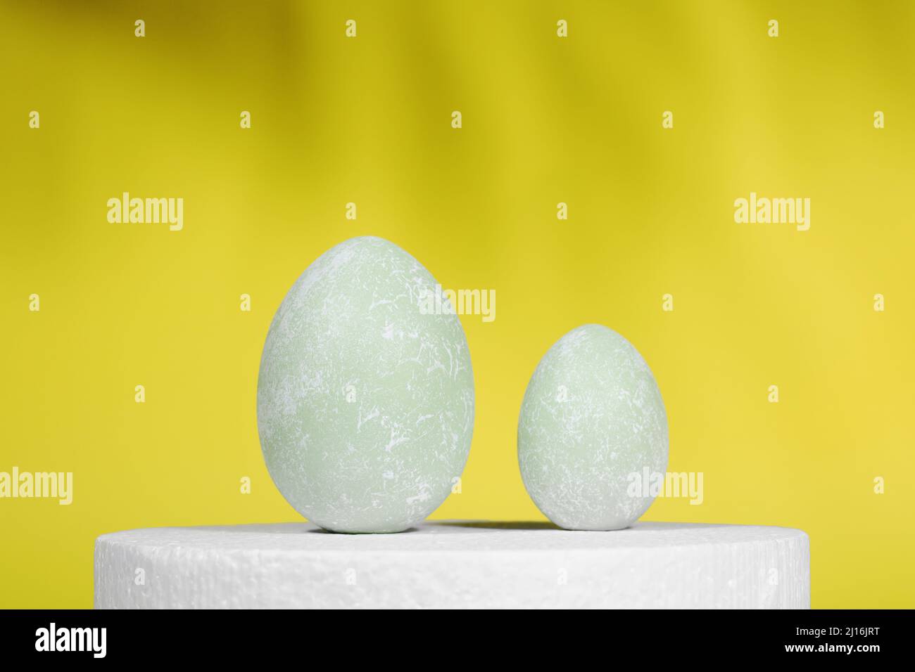 Uova di Pasqua su un supporto bianco, su sfondo giallo con ombre. Sfondo di Pasqua creativo. Minimalismo. Spazio di copia Foto Stock