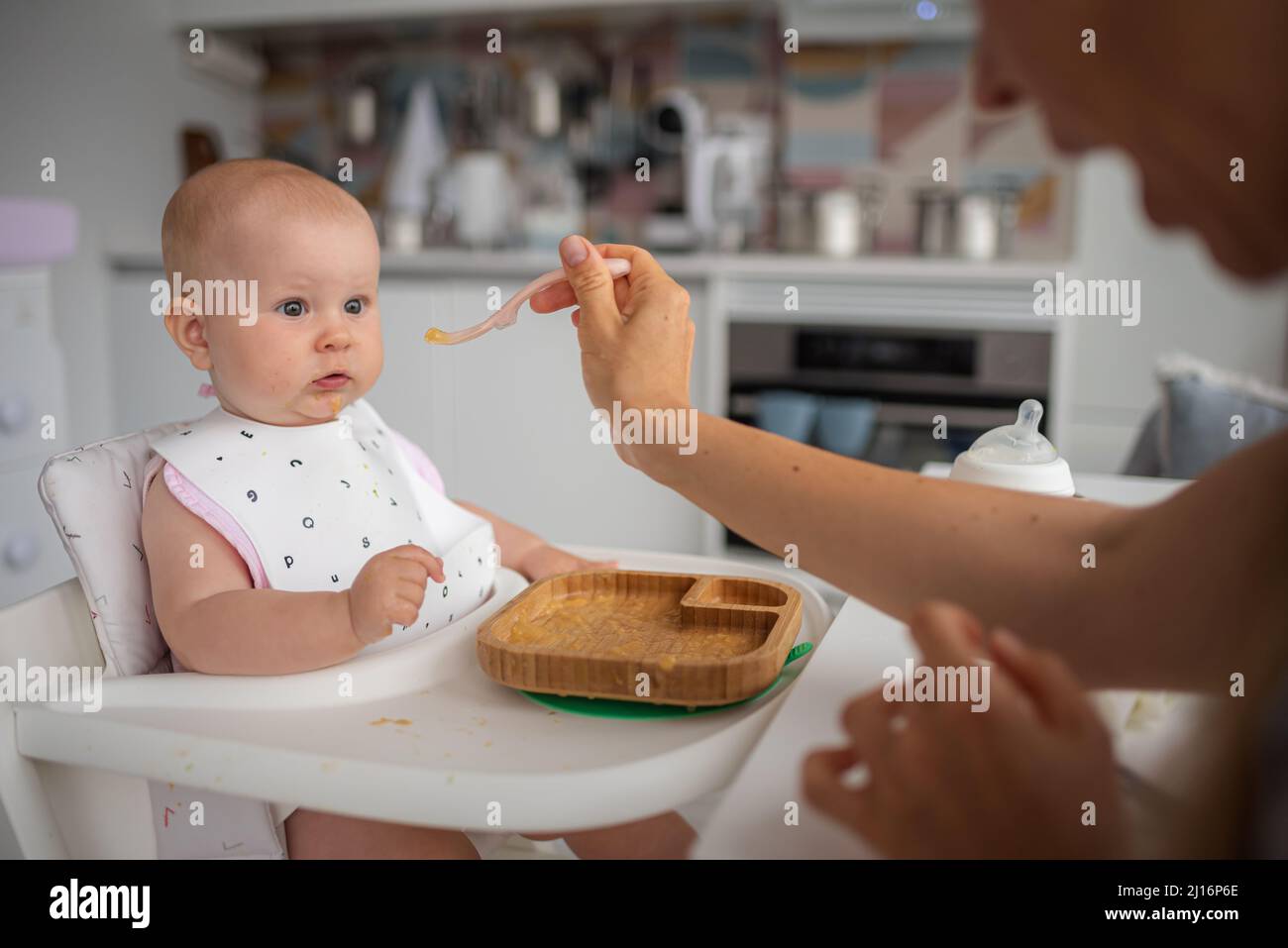 la prima alimentazione del bambino, la mamma nutre un bambino sorpreso con un cucchiaio Foto Stock