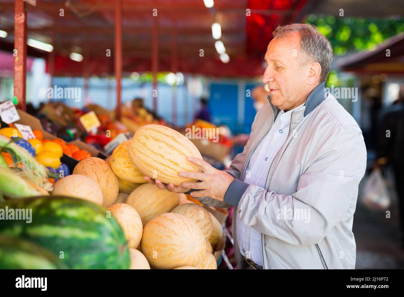 Uomo che sceglie i meloni nel negozio di frutta Foto Stock