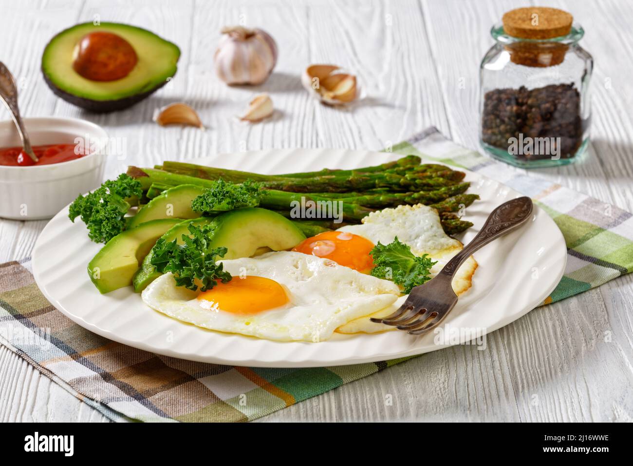 sana colazione di asparagi arrosto, avocado fresco maturo e uova fritte con tuorli runny su un piatto bianco, vista orizzontale, primo piano Foto Stock