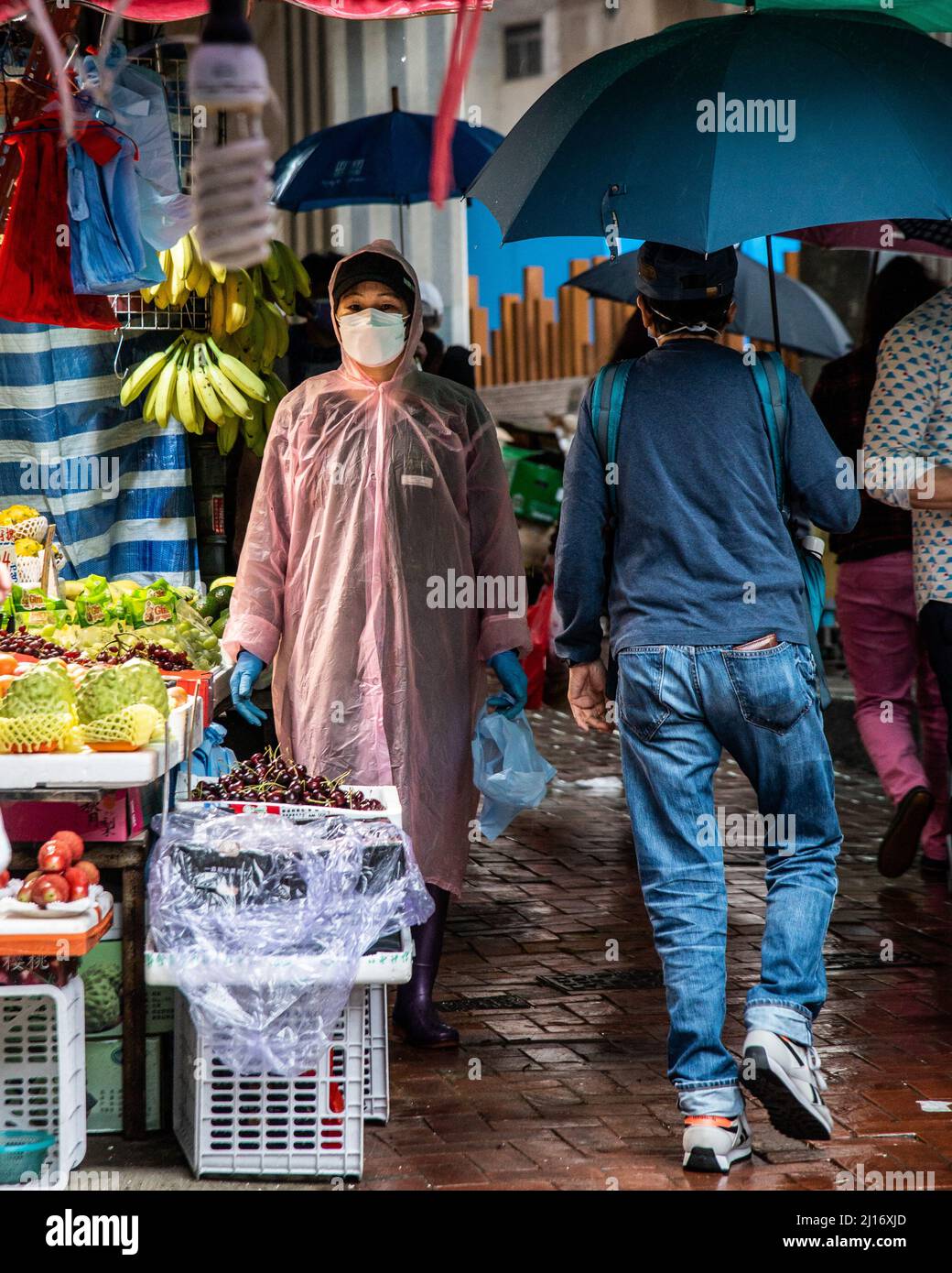 Un lavoratore che indossa un impermeabile aspetta i clienti mentre un monsone settentrionale porta a Hong Kong il clima più fresco e la pioggia. Una giornata di primavera piovosa a Hong Kong. Foto Stock