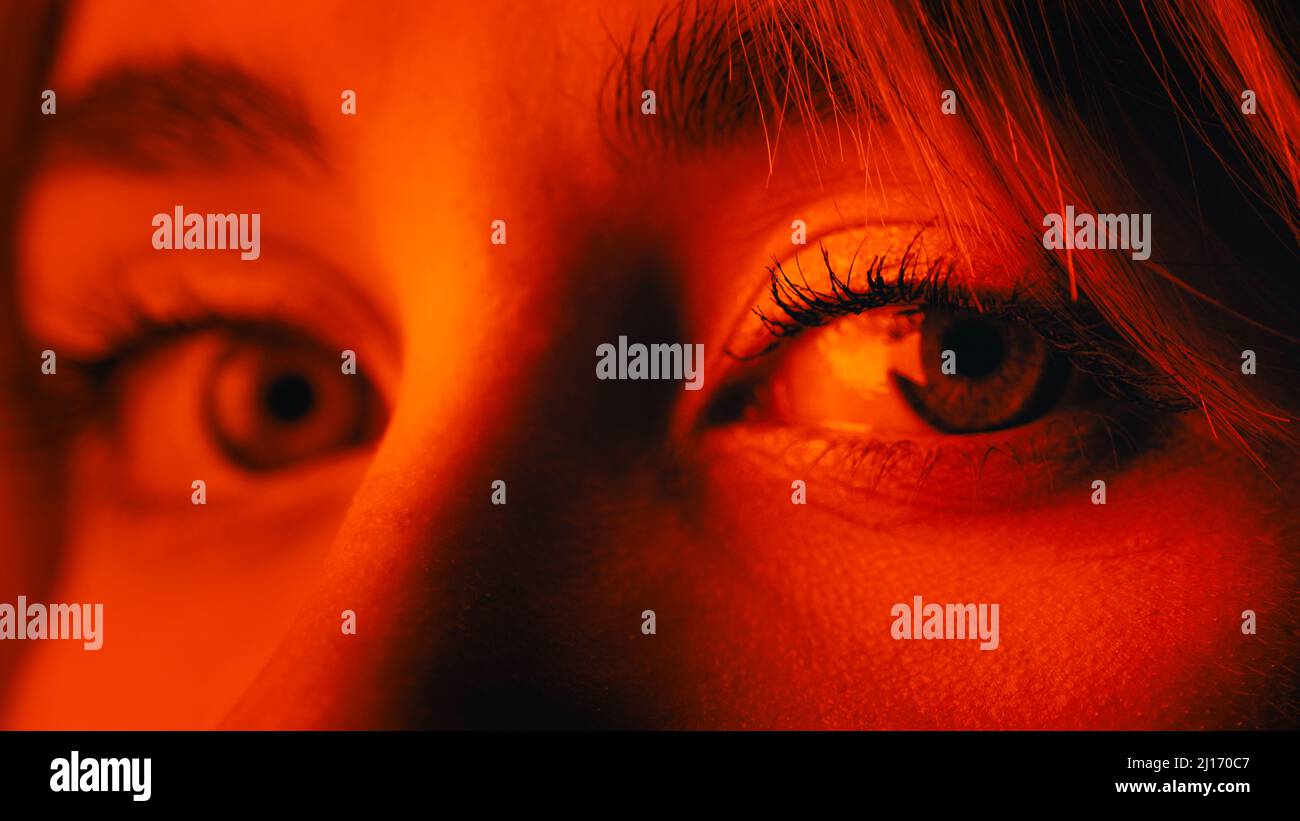 Primo piano di una bella occhio blu femmina sguardo su luce rossa Foto Stock