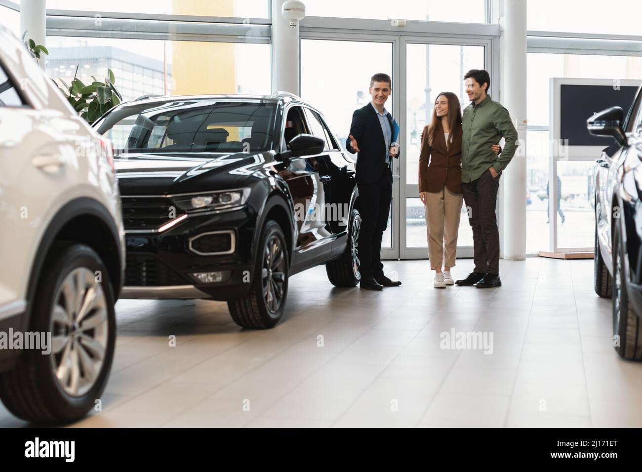 Un venditore fiducioso che mostra la nuova auto alla giovane coppia caucasica presso la concessionaria auto Foto Stock