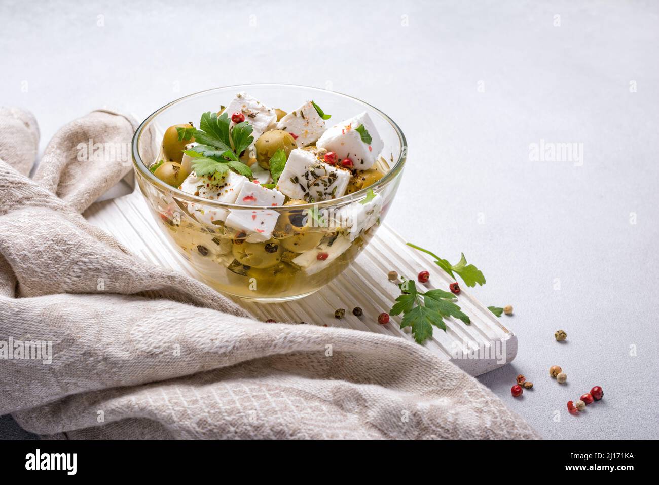 Gustose olive verdi con formaggio Feta, pepe e prezzemolo fresco in recipiente di vetro con olio su fondo di cemento grigio Foto Stock