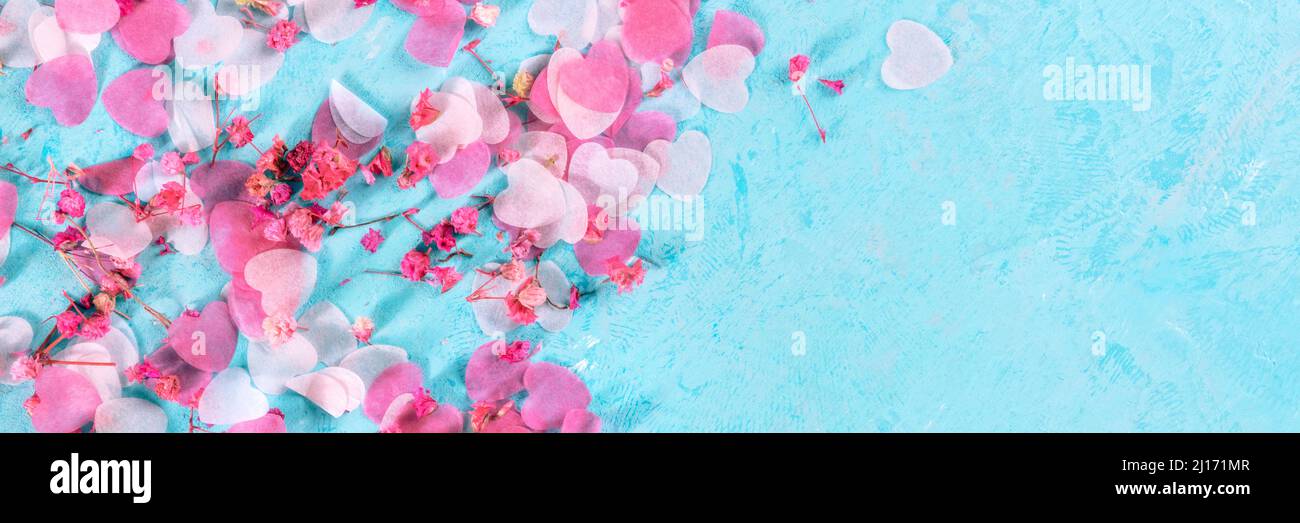 Panorama di San Valentino con cuori rosa e fiori di confetti, un banner panoramico piatto e posato su sfondo blu con un posto per il testo Foto Stock