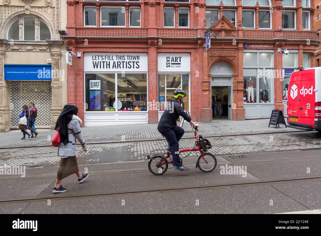 Ciclista sulla linea tranviaria evitando gli amanti dello shopping nel centro di Birmingham Foto Stock